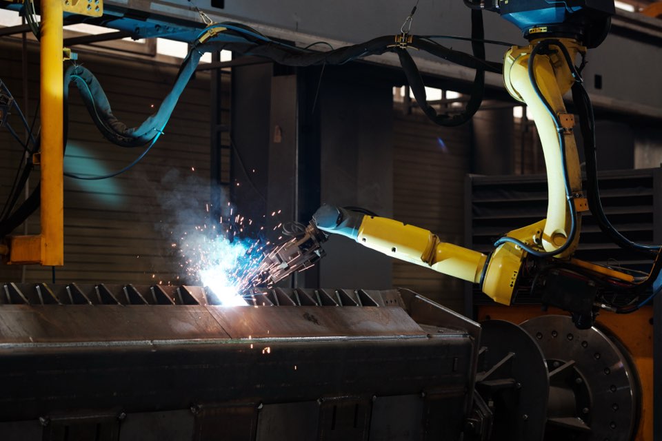 Arc welding of part of huge iron industrial automated machine during process of repairing inside machinery production plant