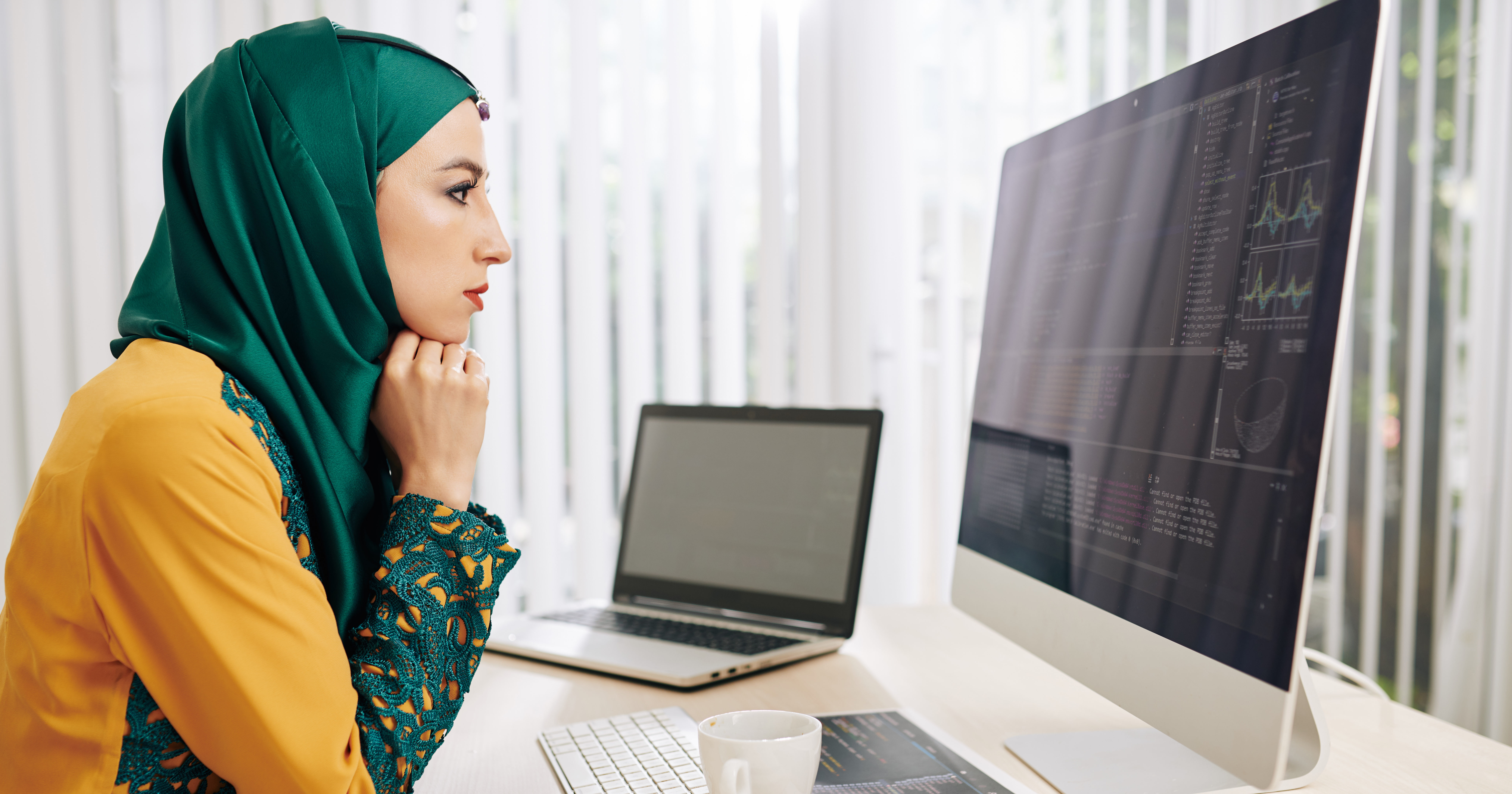 Frowning serious female muslim coder looking for mistakes in her programming code on computer screen