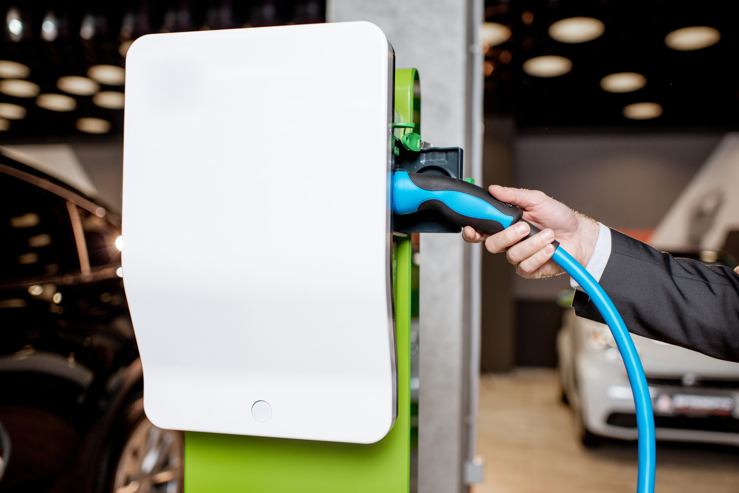 Man plugging cable into the charging station for electric cars at the car dealership, close-up view